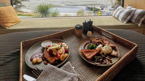 A breakfast tray with pancakes and fruit on a bed with a view of mountains and a river. - EcoScapes (Kinloch)