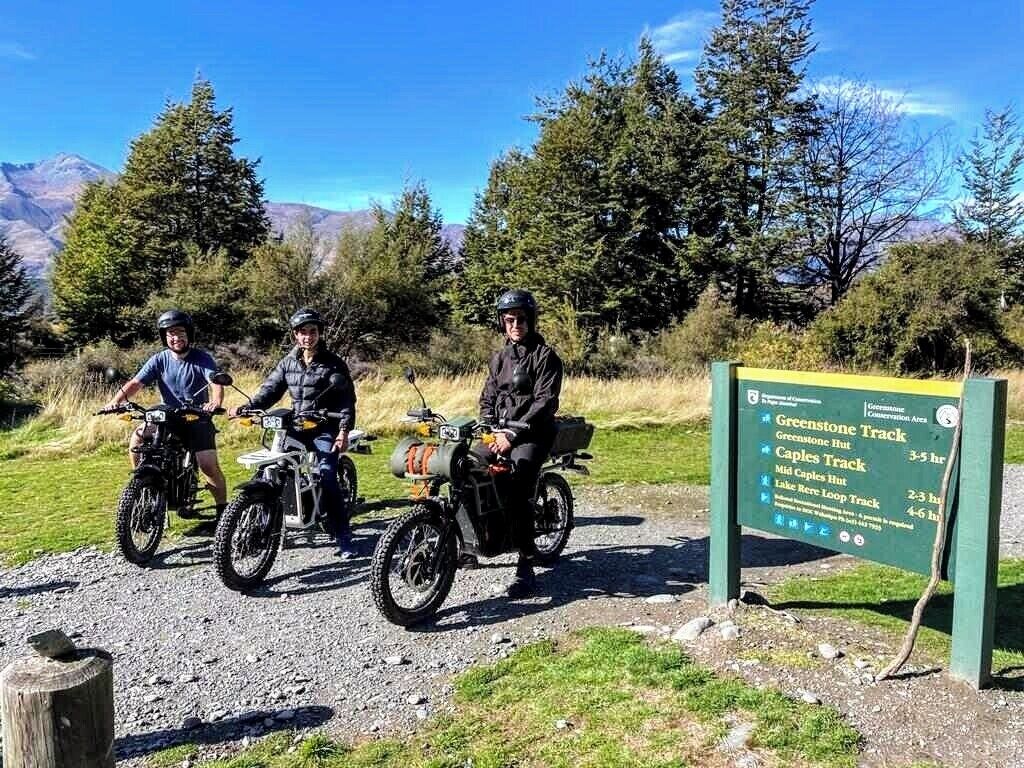 Three people on ATVs in a natural setting with a sign indicating trails.