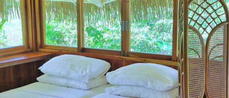 Una habitación con dos camas, paredes de madera y ventanas amplias que dan a un jardín exuberante.