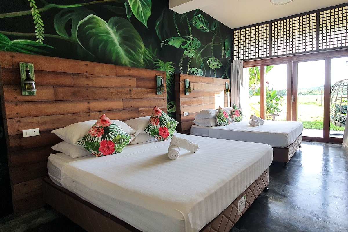 Habitación de hotel con una cama grande, una cama más pequeña, cabecero de madera y un mural de plantas tropicales.