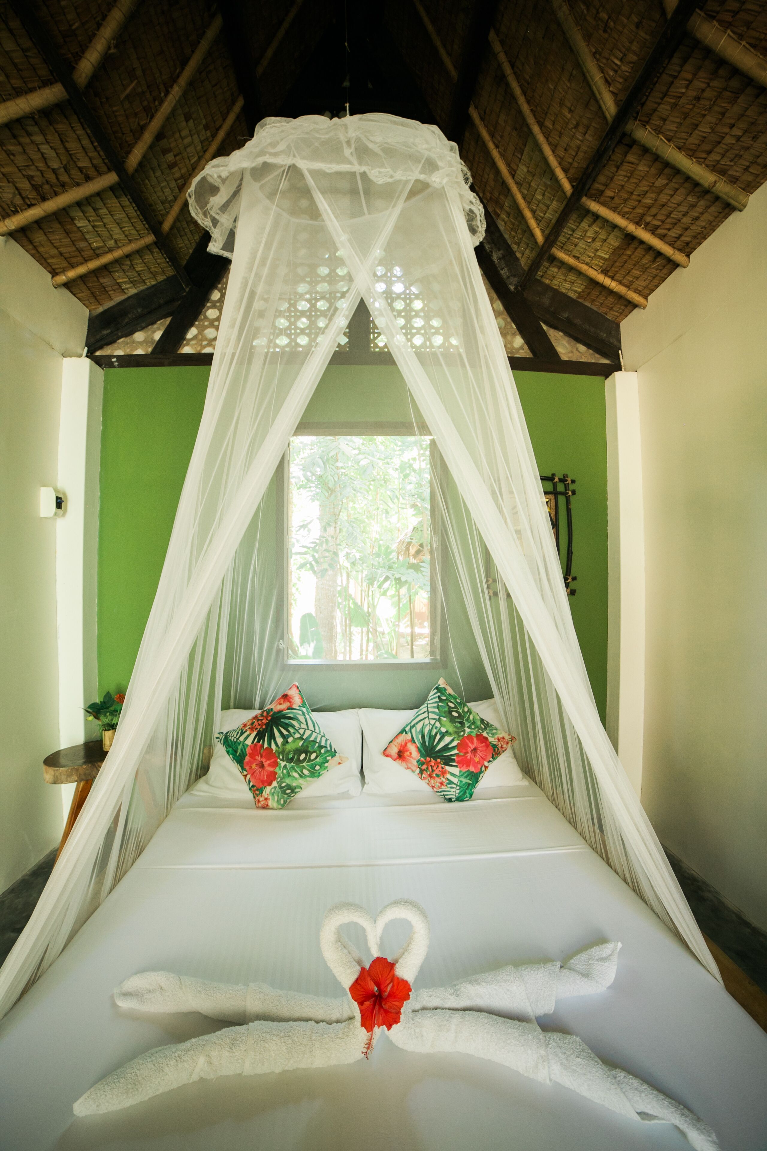 A bed with a canopy, two pillows with tropical designs, and a heart-shaped towel arrangement.