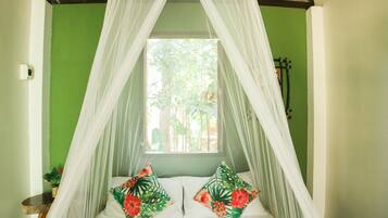 A bed with a canopy, two pillows with tropical designs, and a heart-shaped towel arrangement.