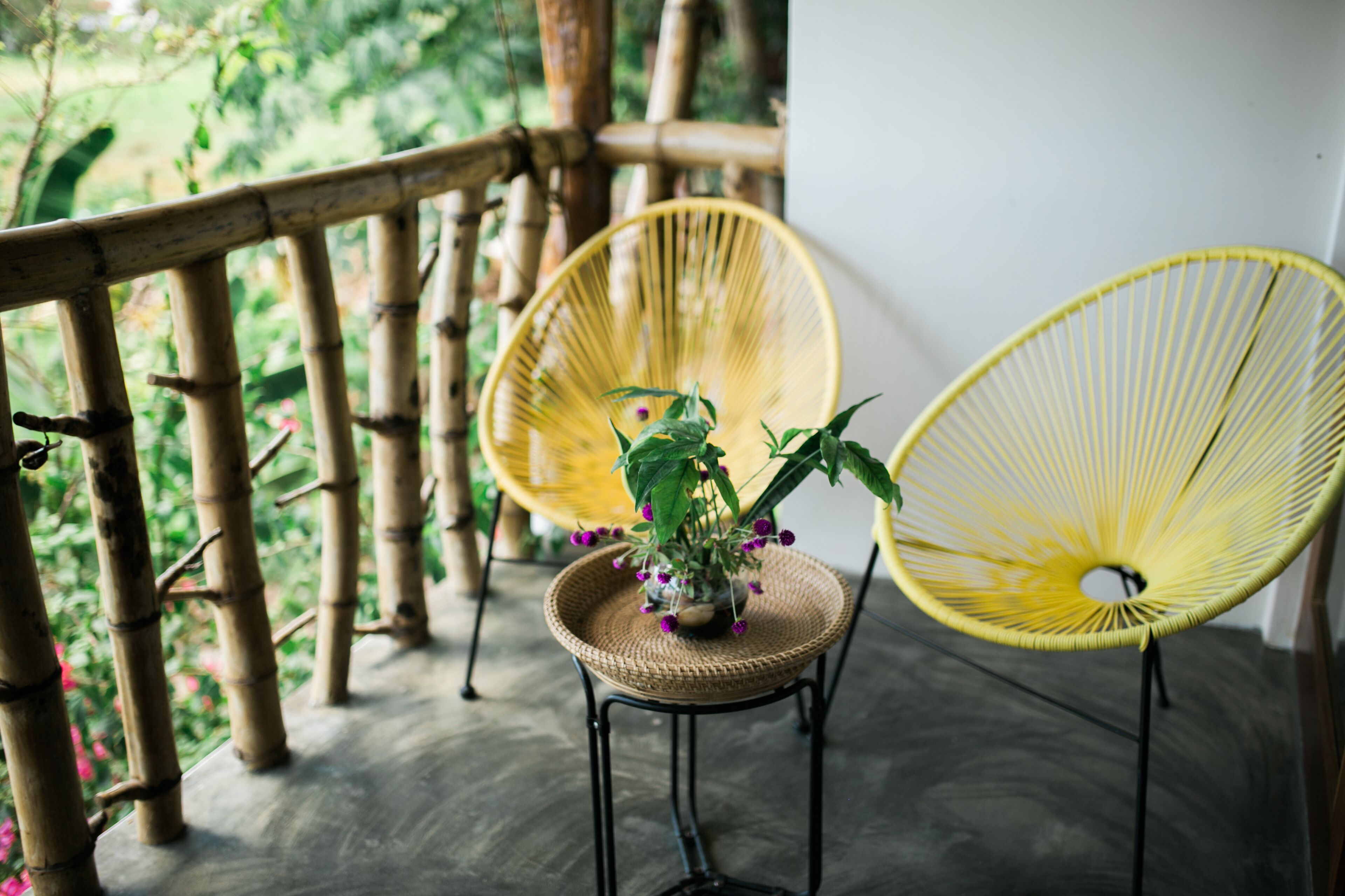 Un balcon en bois avec deux fauteuils en osier et une petite table sur laquelle est posée une plante en pot.