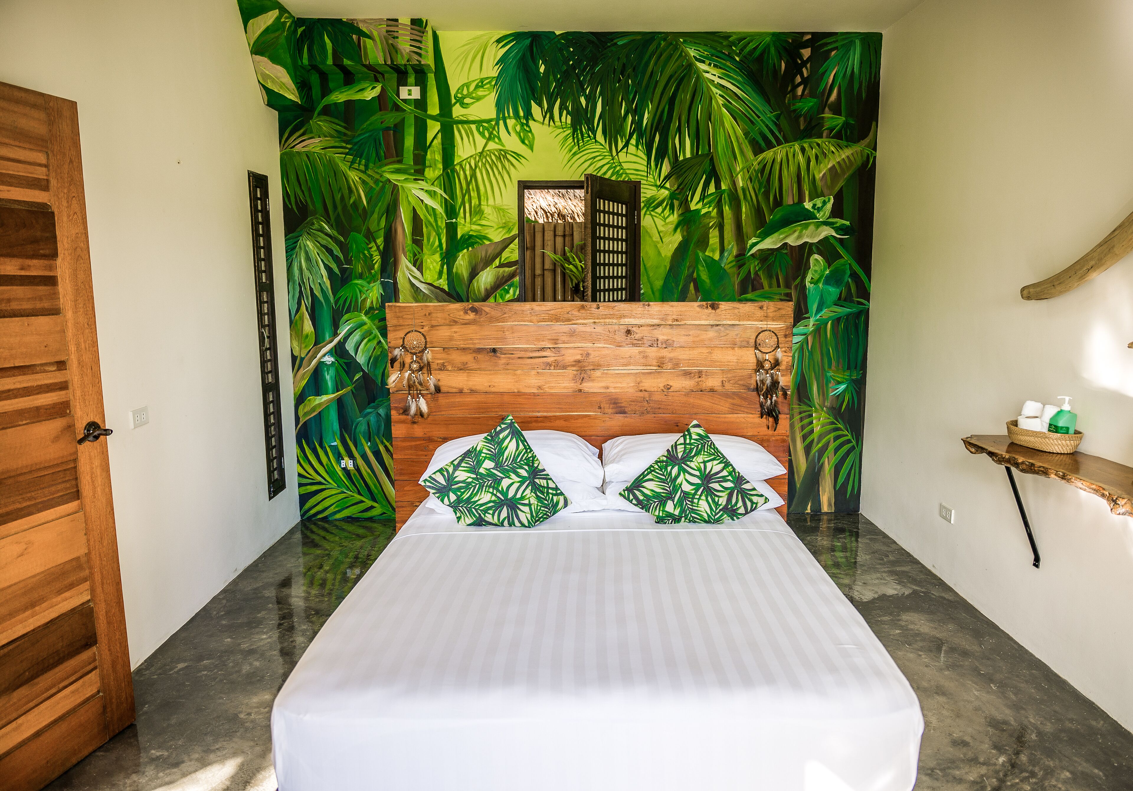 Un dormitorio con cama, cabecera de madera y un mural tropical en la pared.