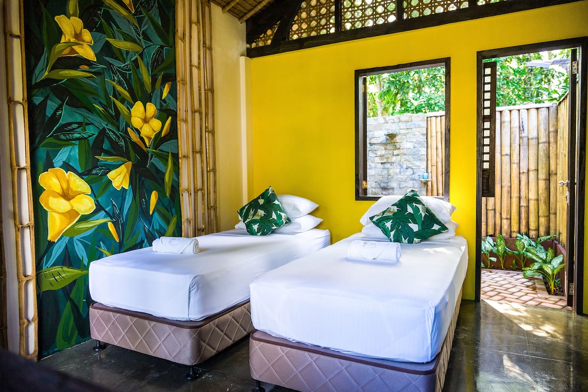 Una habitación con dos camas, una pared amarilla y un mural de flores amarillas.