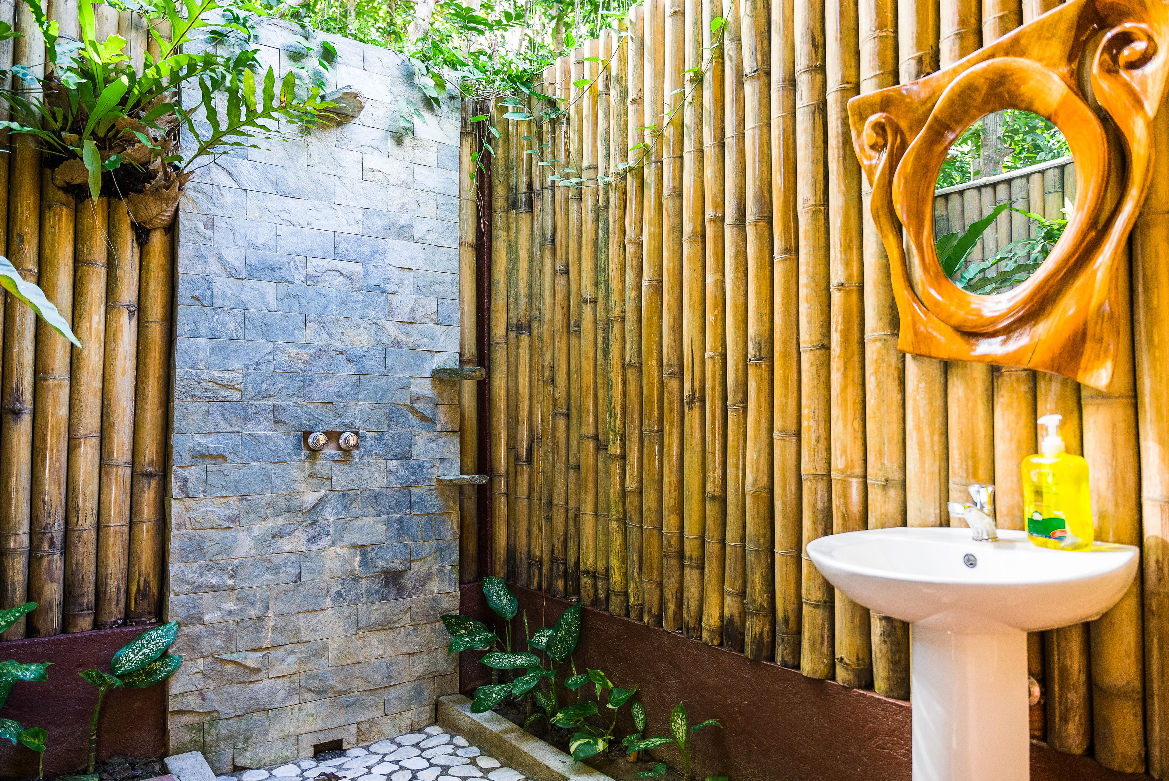 A bathroom with a stone wall, bamboo fence, and a white sink with a mirror.