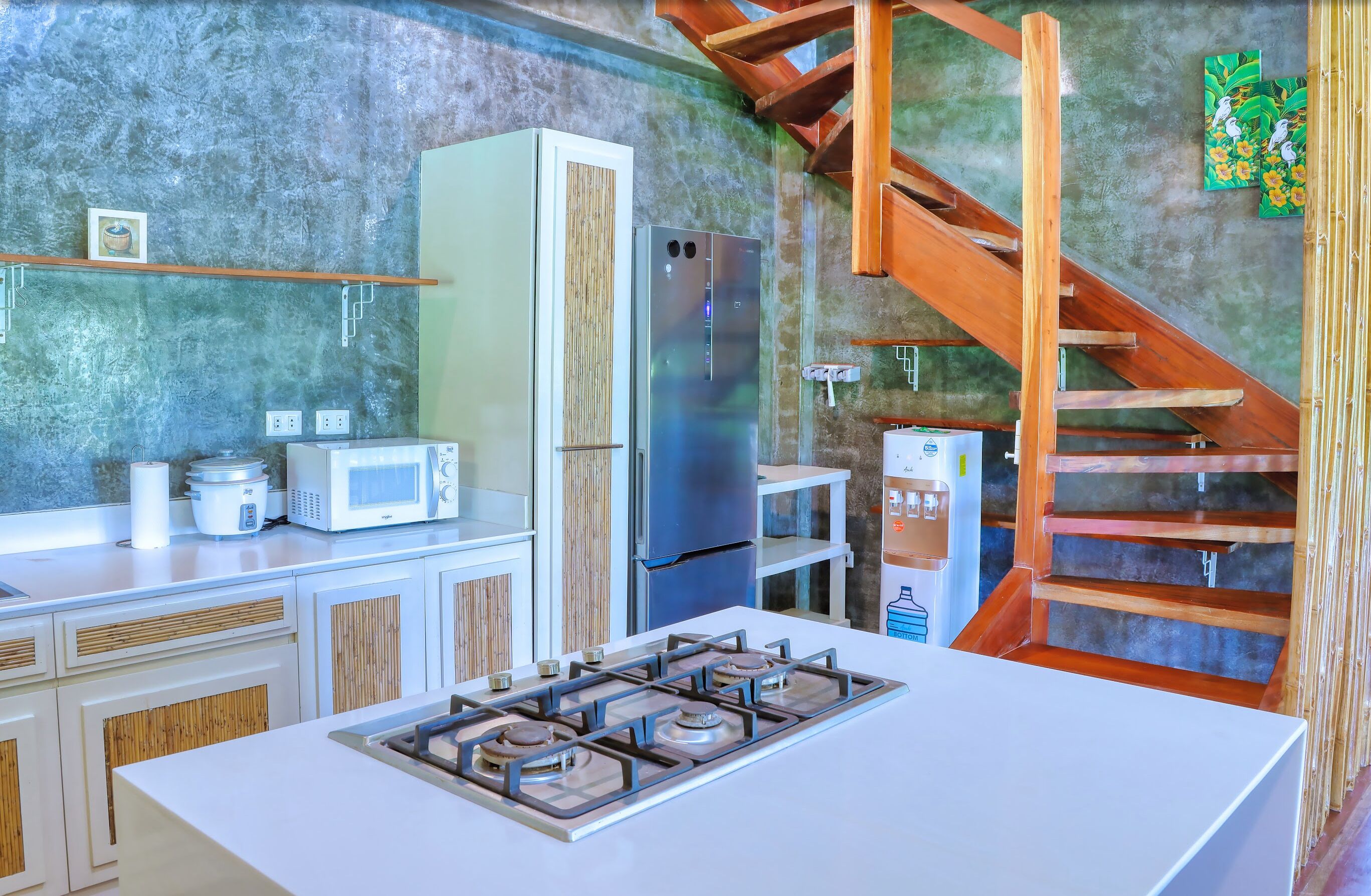 Una cocina con estufa a gas, armarios blancos, microondas, refrigerador y una escalera de madera.