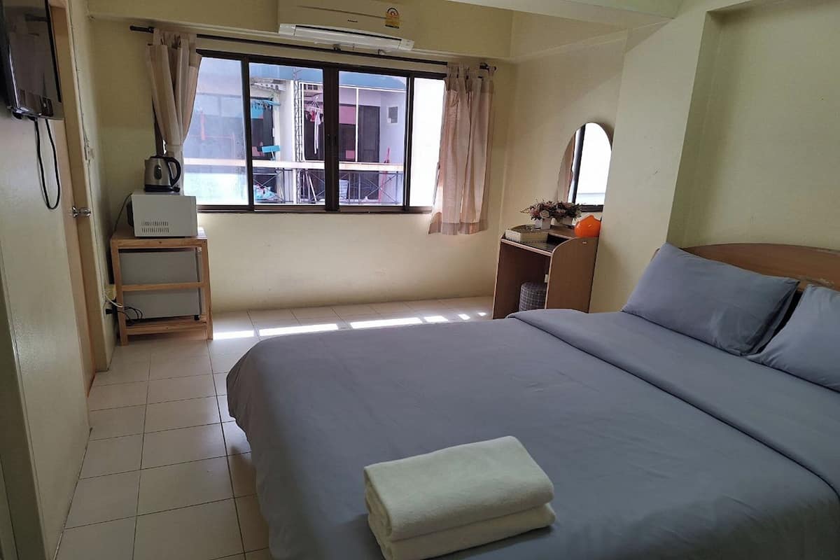 A hotel room with a bed, a desk, a window with curtains, and a view of buildings outside.