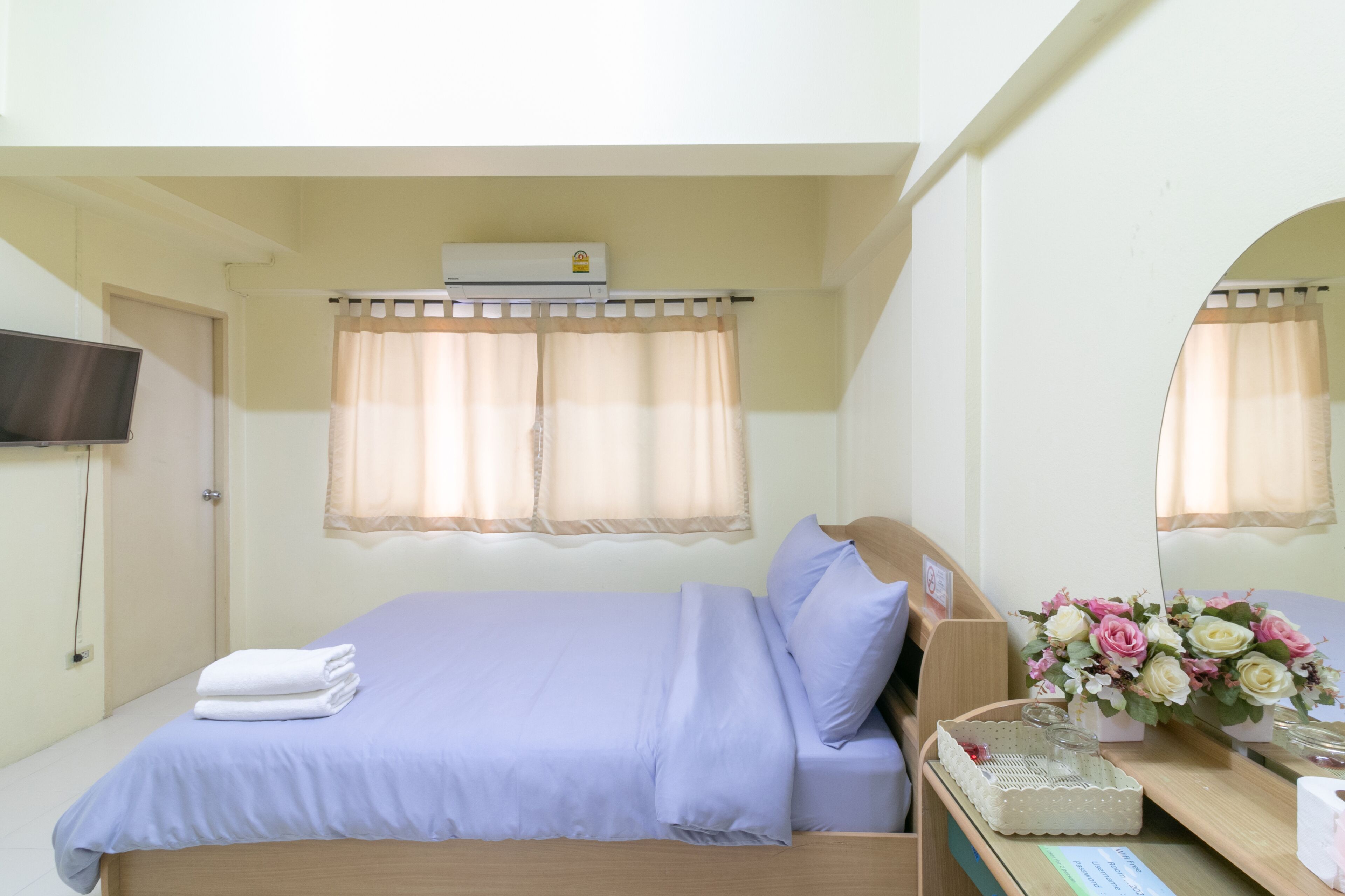 A hotel room with a bed, a flat-screen TV, a window with curtains, and a mirror.