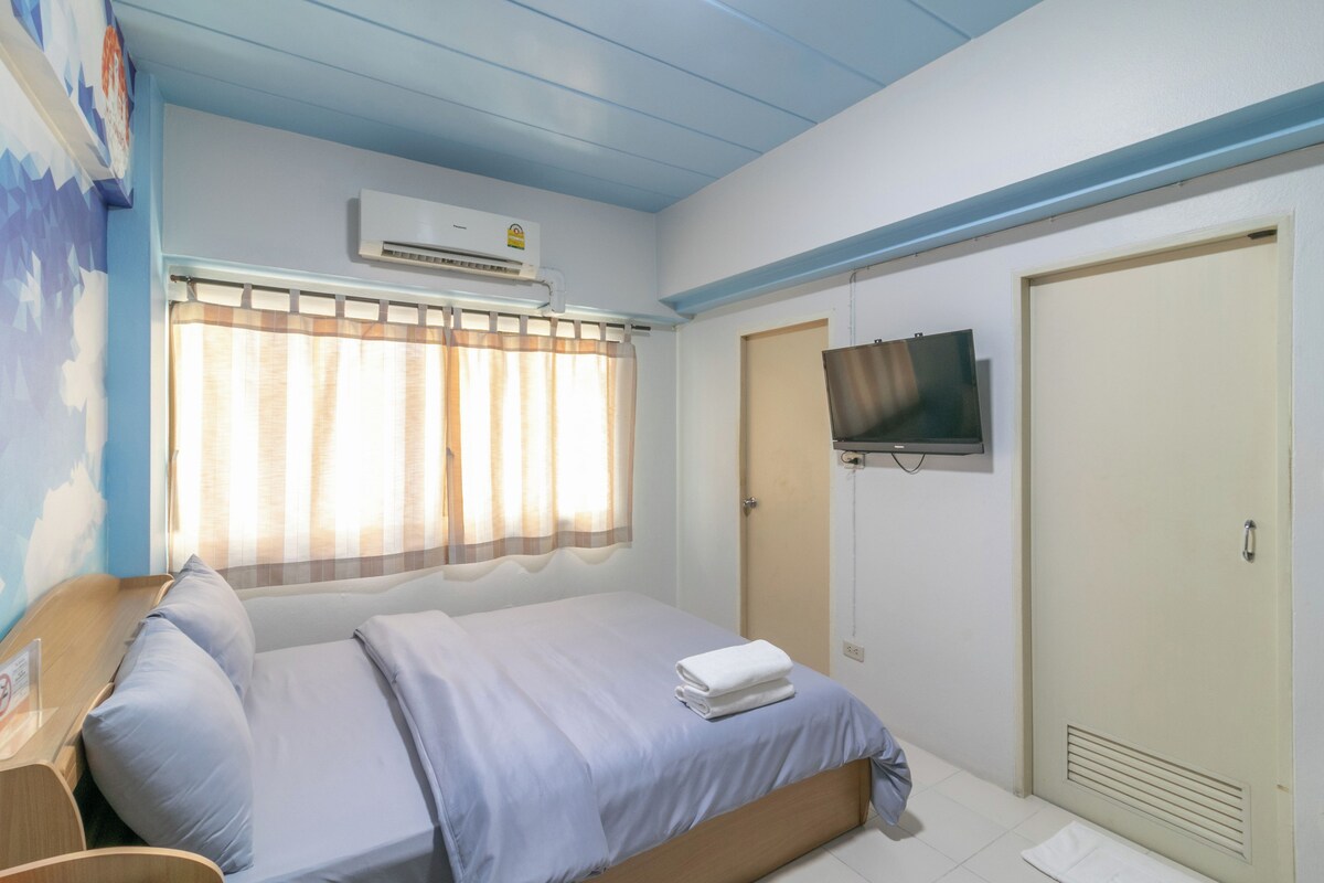 Une chambre d’hôtel équipée d’un lit, d’un téléviseur fixé au mur, d’une fenêtre avec des rideaux et d’un appareil de climatisation.