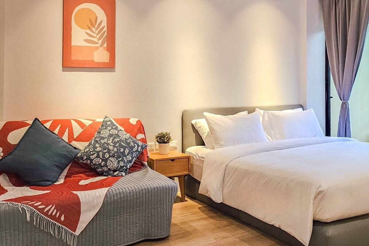 Un dormitorio con cama, sofá, mesita de noche y ventana con cortinas.
