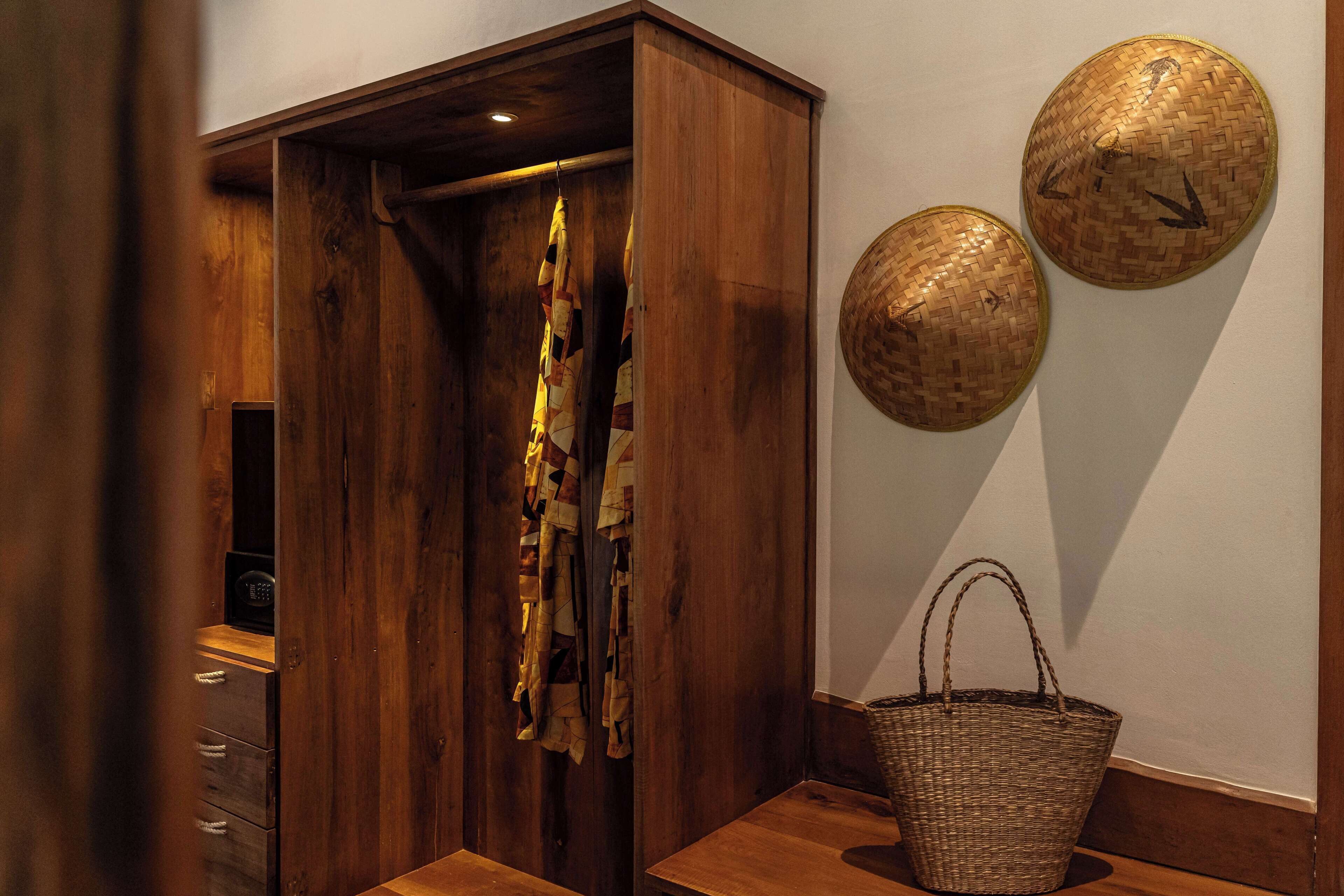 A wooden wardrobe with a hanging garment, a wicker basket, and two woven wall decorations.