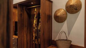 A wooden wardrobe with a hanging garment, a wicker basket, and two woven wall decorations.