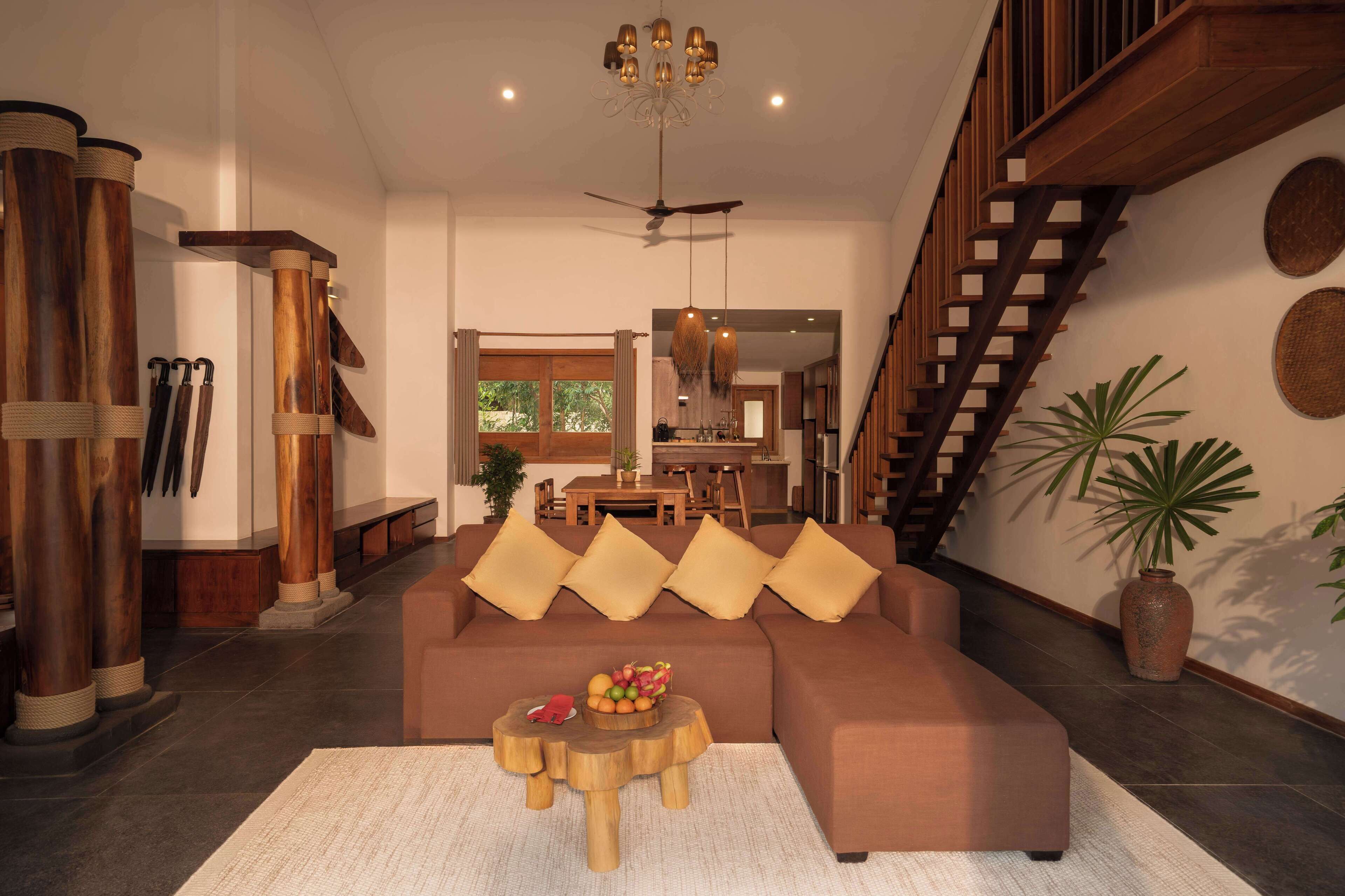 A spacious living room with a brown sofa, wooden columns, a dining area, and a staircase.