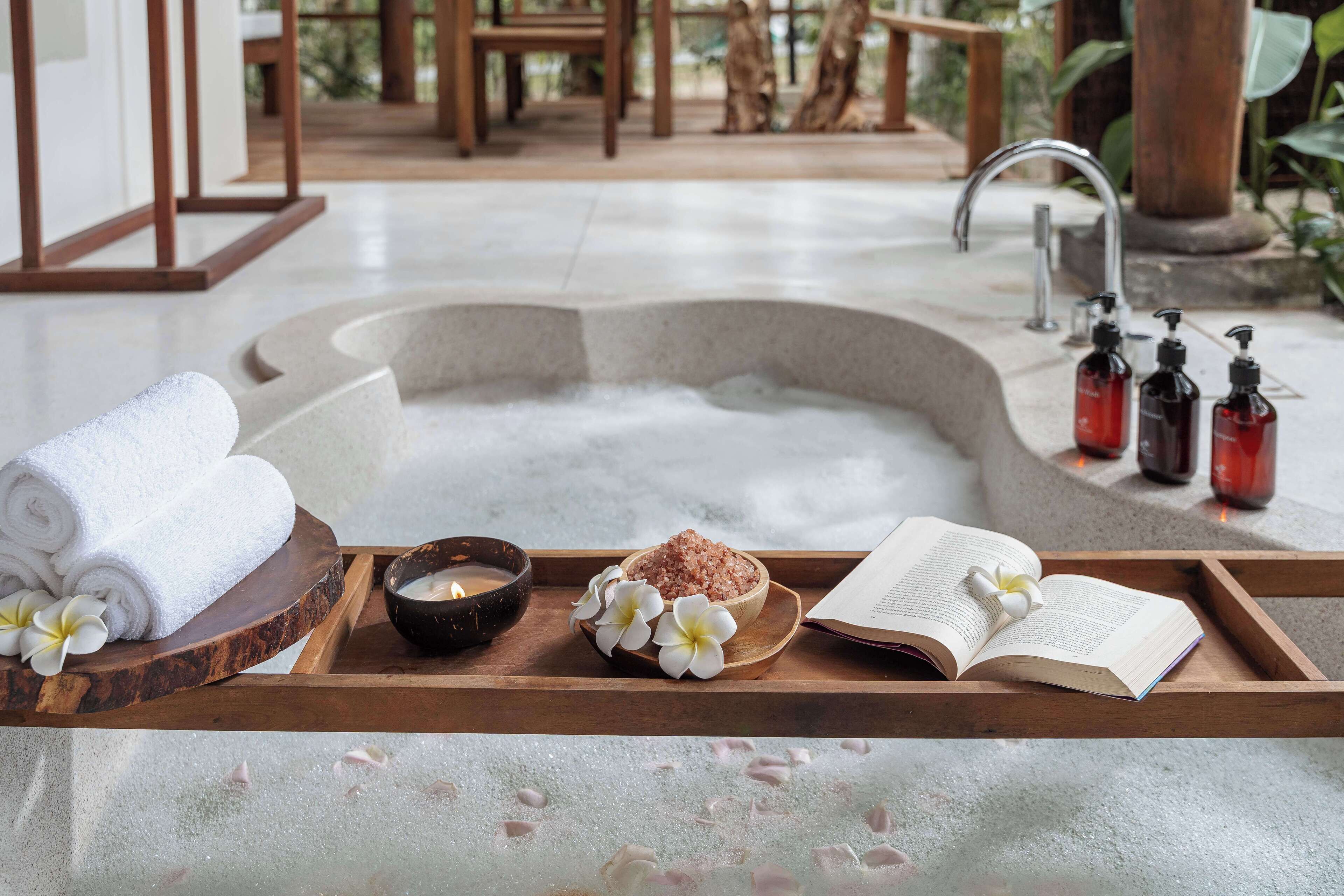 A spa area with a hot tub, towels, a book, and bath salts on a wooden tray.