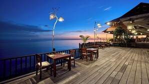 A wooden deck with tables and chairs, overlooking a body of water at dusk. - Green Bay Phu Quoc Resort & Spa (Phu Quoc)