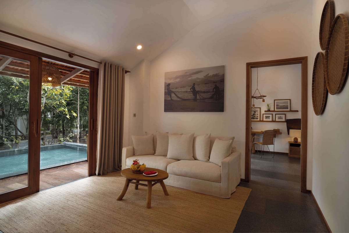 Una sala de estar con sofá, una mesa de centro con fruta, un cuadro y vistas a una piscina.
