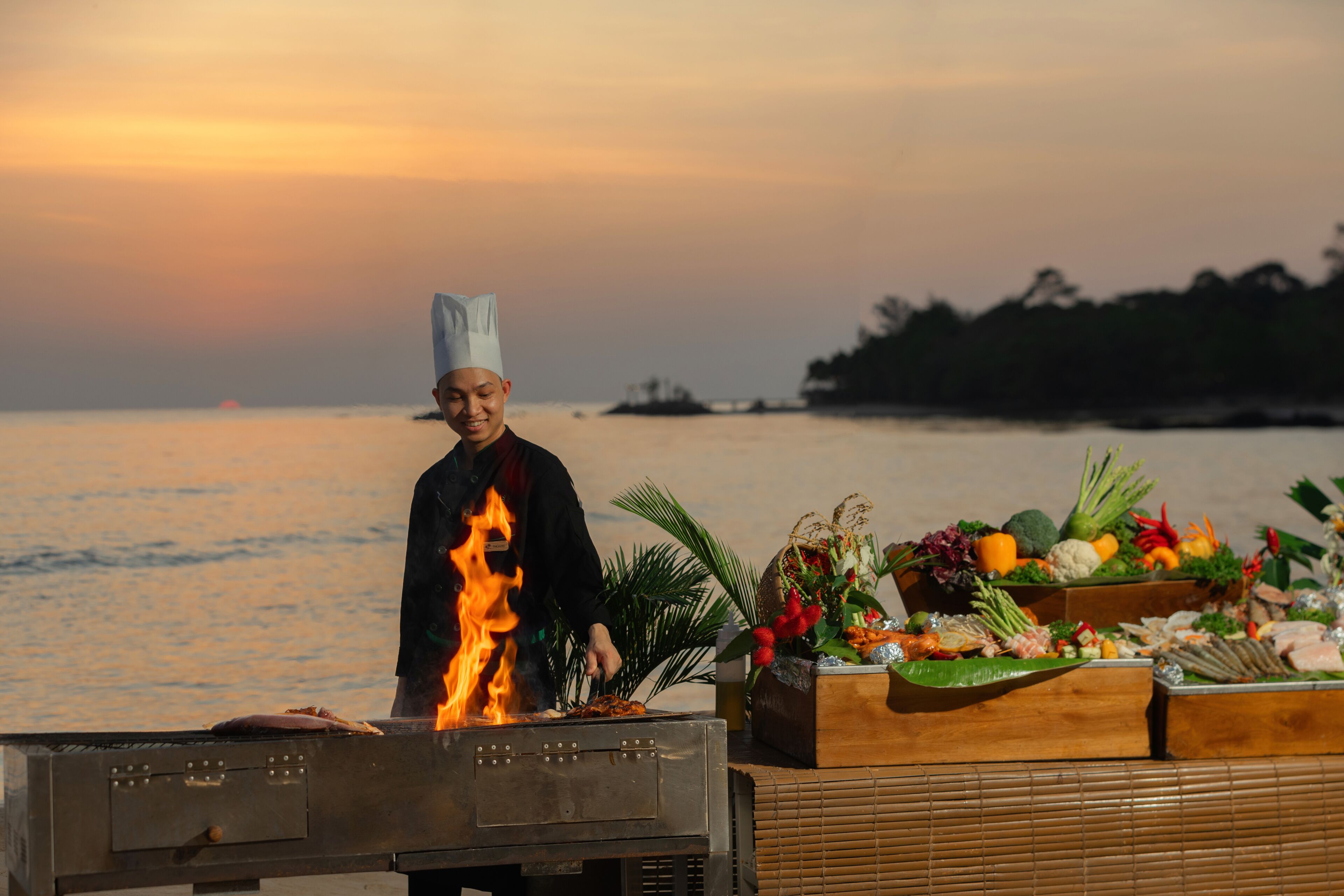 Un chef cocina al aire libre, con una barra de vegetales y carnes de fondo.