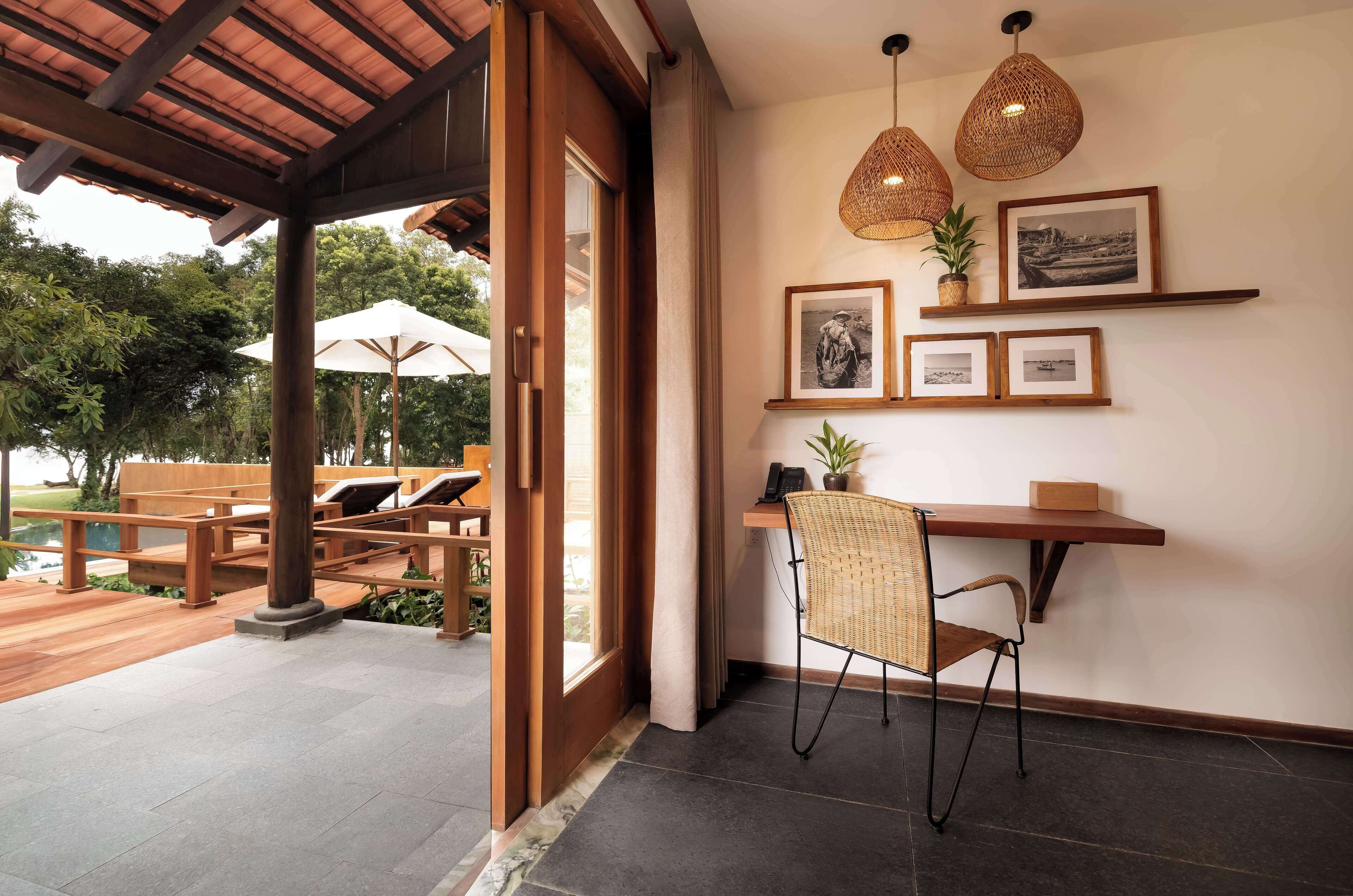 An indoor seating area with wooden benches and a table, a wicker chair, and a shelf with framed pictures and a plant.