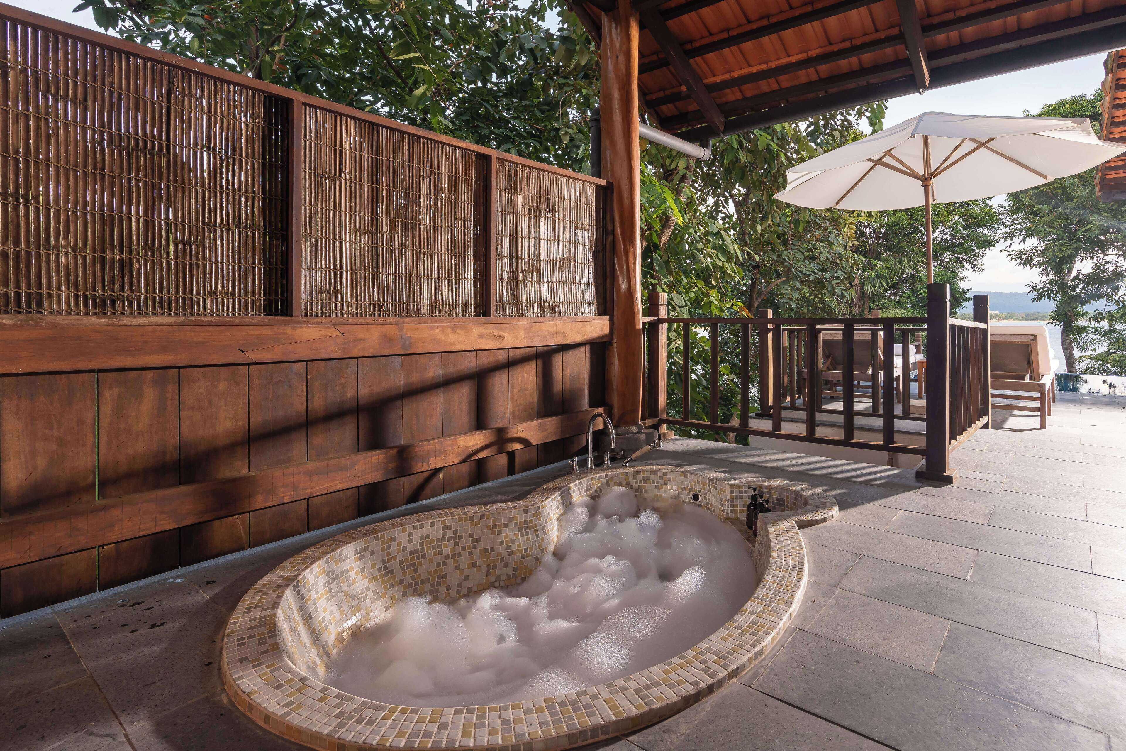 A hot tub with mosaic tiles, wooden walls, and a covered seating area with an umbrella.