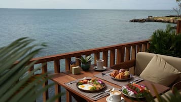 Una mesa de madera con platos de comida, una taza de café y vista al mar.