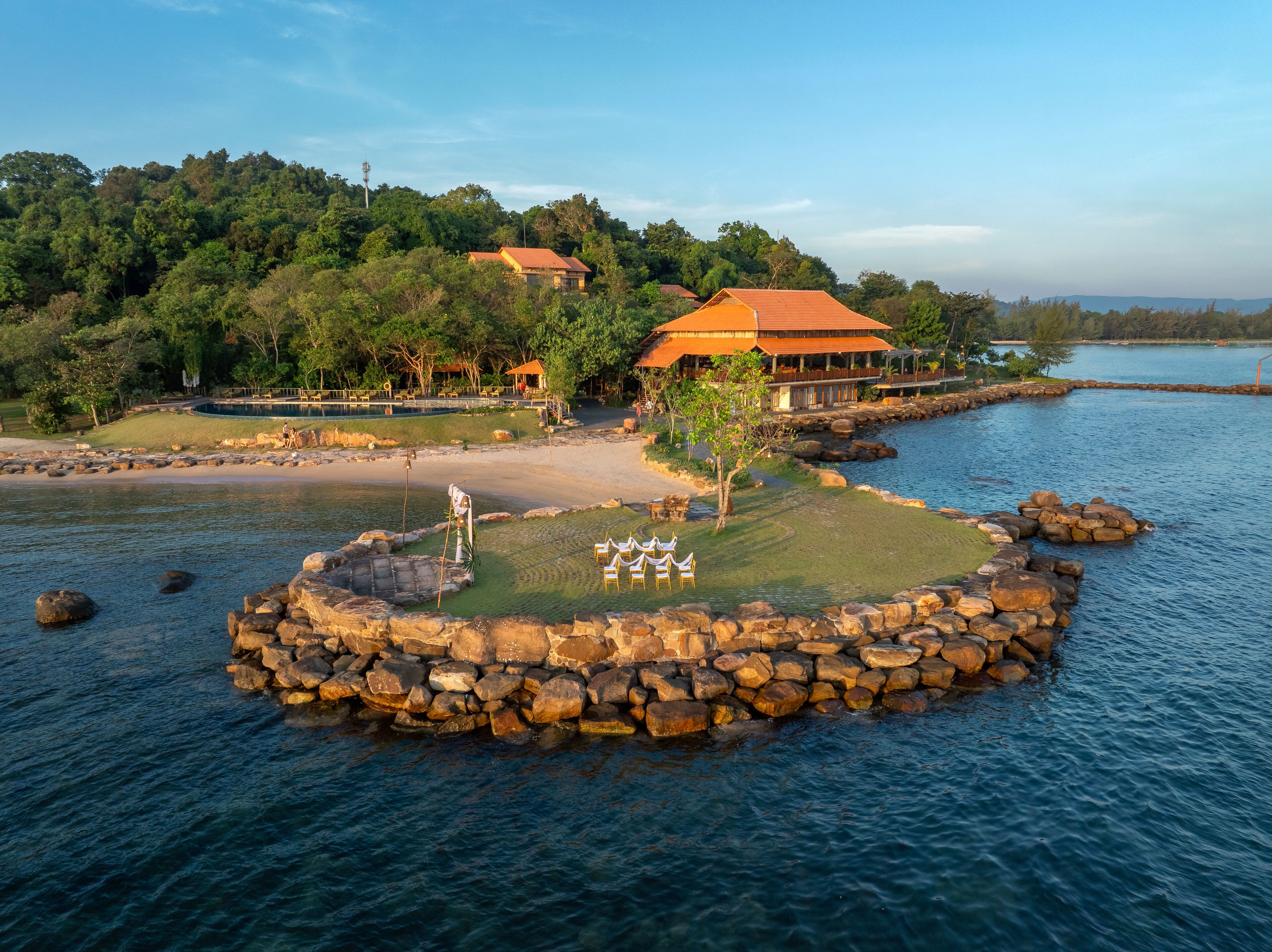 A lakeside property with a stone dock, a grassy area with chairs, and a building with a red roof.