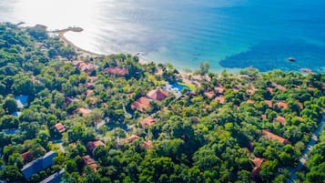 An aerial view of a coastal residential area with houses surrounded by dense greenery and a clear blue sea.