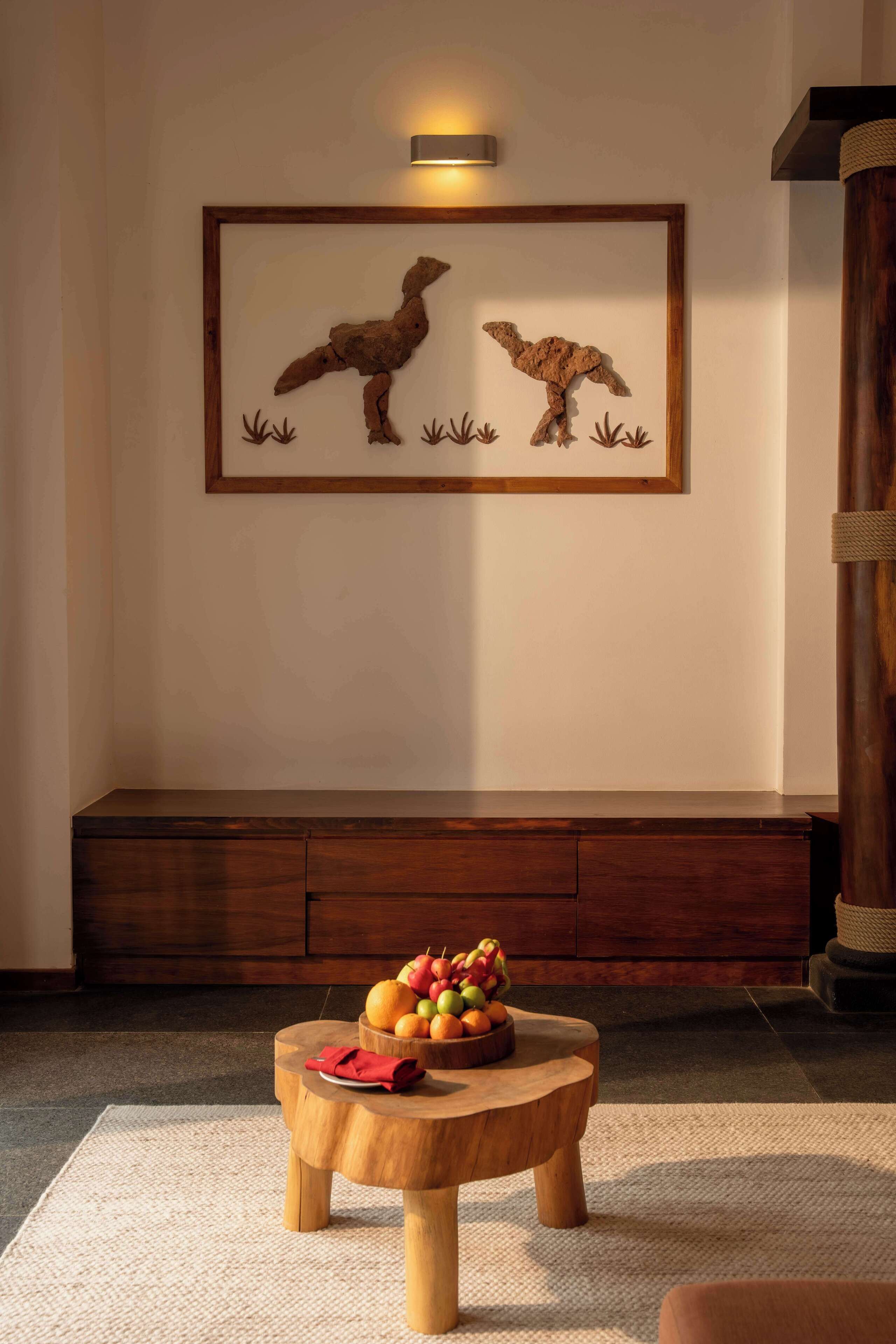 A room with a wooden bench, a small round table with fruit, and a framed artwork on the wall.