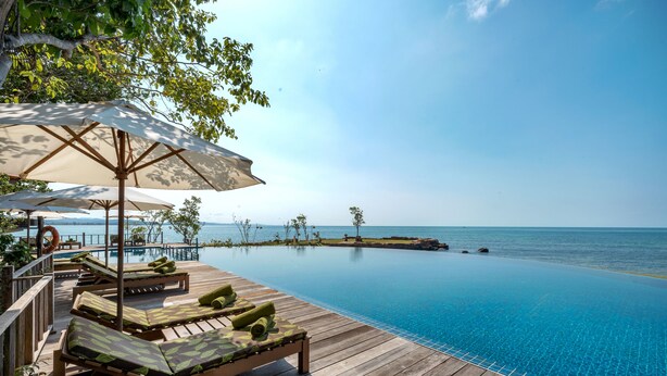 A wooden deck with lounge chairs and umbrellas overlooking a clear blue pool and the sea. - Green Bay Phu Quoc Resort & Spa (Phu Quoc)