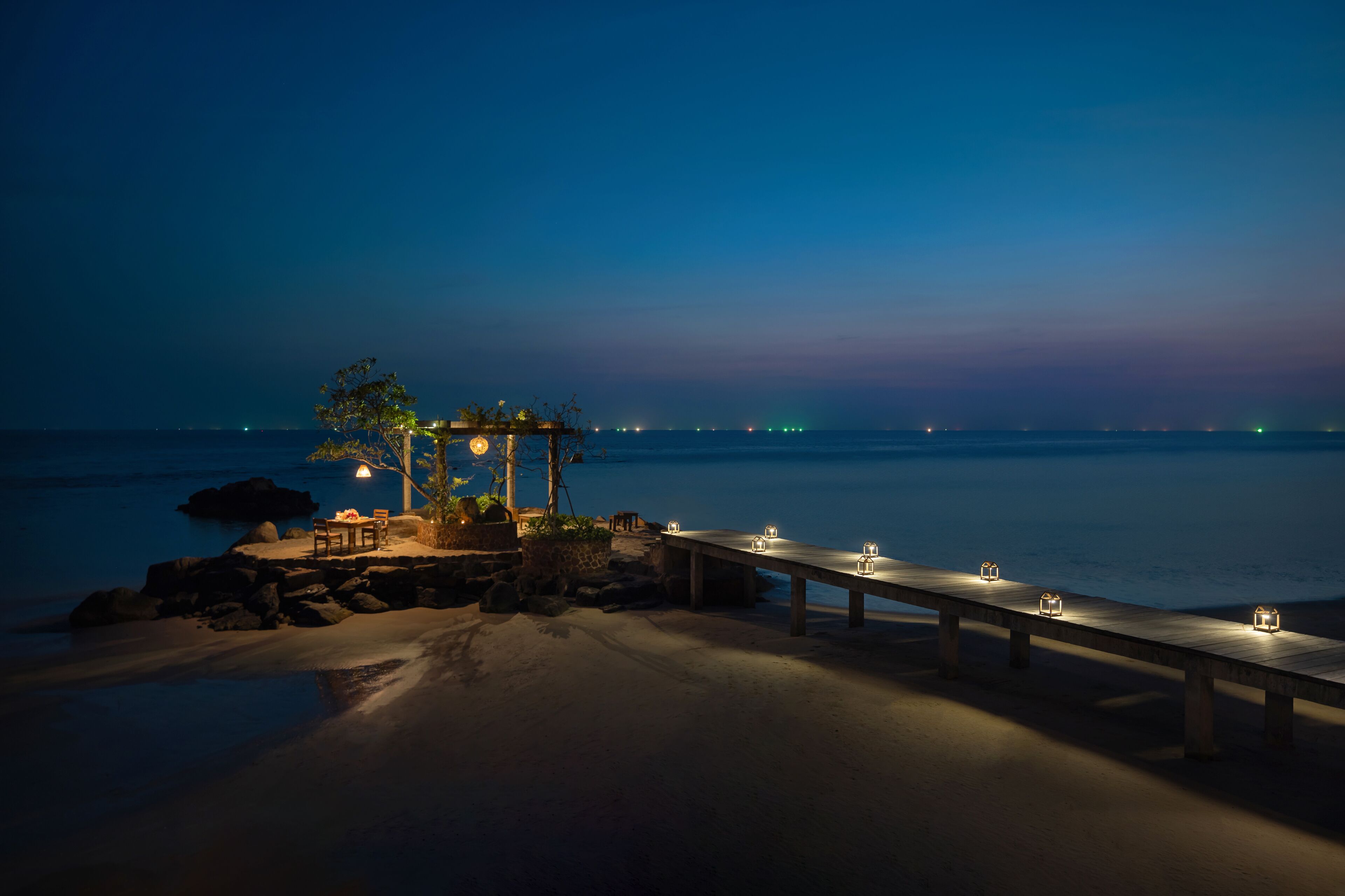 A beachside deck with a wooden bench and a small gazebo, overlooking the ocean.