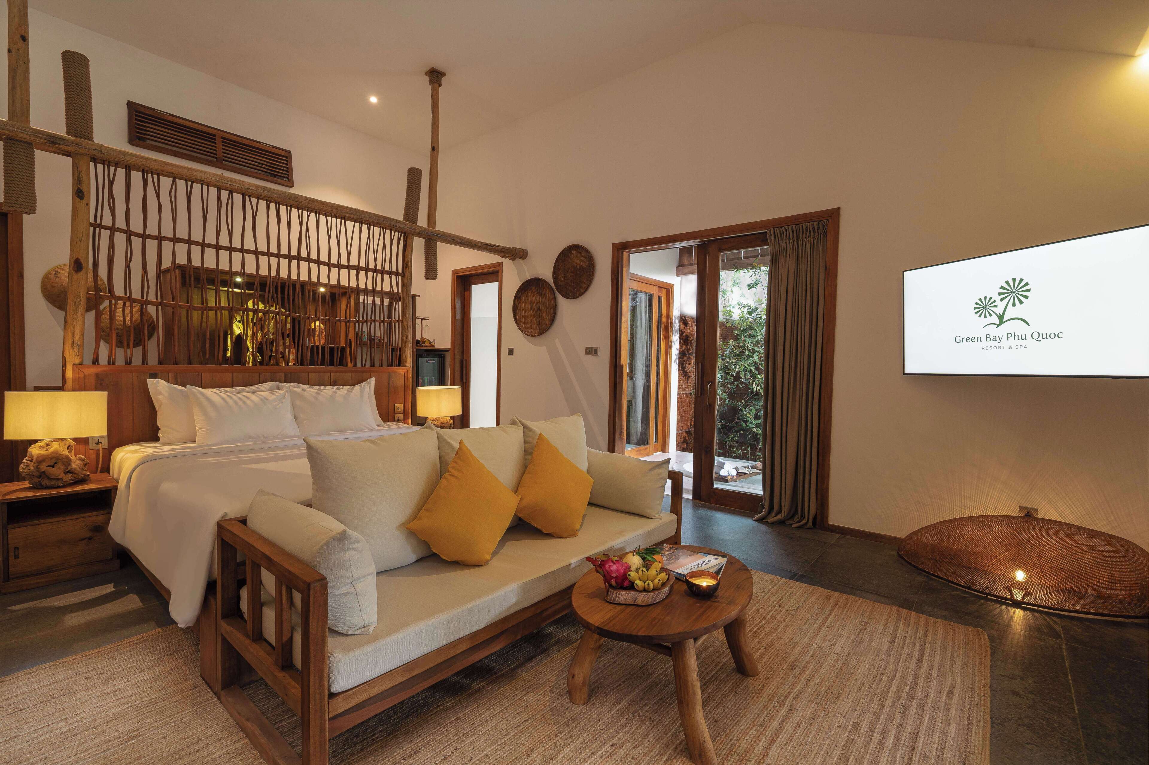 A hotel room with a bed, a sofa, a small table with fruit, and a TV displaying the hotel name.
