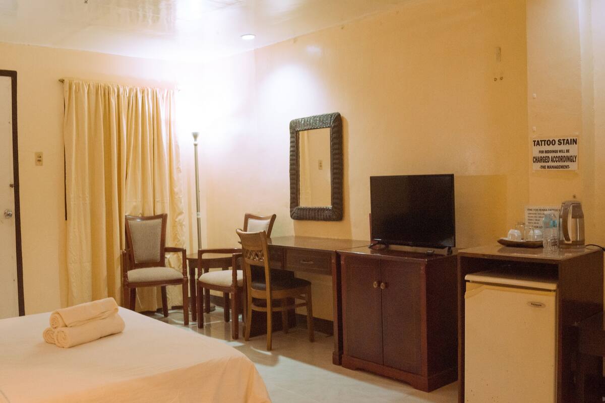 A hotel room with a bed, a desk with a television, a small refrigerator, and a mirror on the wall.