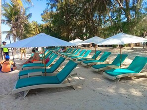 En la playa, arena blanca, sillas reclinables de playa, sombrillas