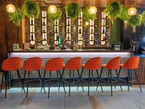 A bar area with a counter, bar stools, and a wall of shelves with bottles. - ONOMO Hotel Johannesburg Sandton (Sandton)
