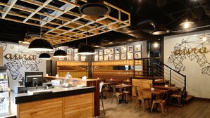 A restaurant interior with wooden furniture, a counter, and framed pictures on the walls. - ONOMO Hotel Johannesburg Sandton (Sandton)