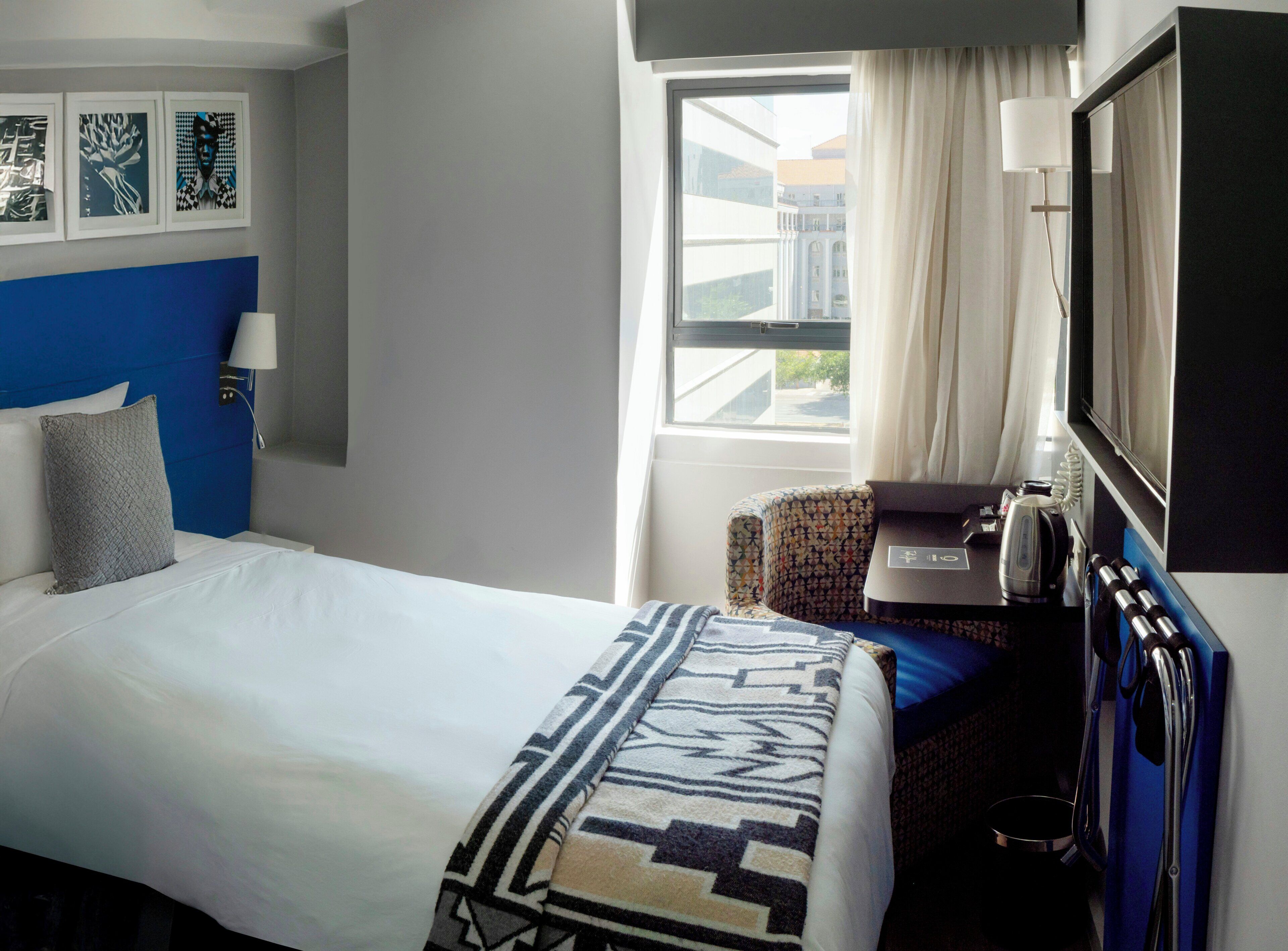 A hotel room with a bed, a desk with a computer, a chair, a TV, and a window with curtains.