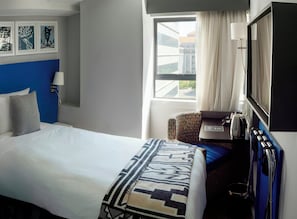 Habitación de hotel con cama, escritorio con computadora, silla, televisor y ventana con cortinas.