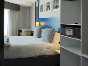 A hotel room with a bed, bedside tables, a lamp, a nightstand, a shelf with a remote control, and framed artwork on the wall. - ONOMO Hotel Johannesburg Sandton (Sandton)