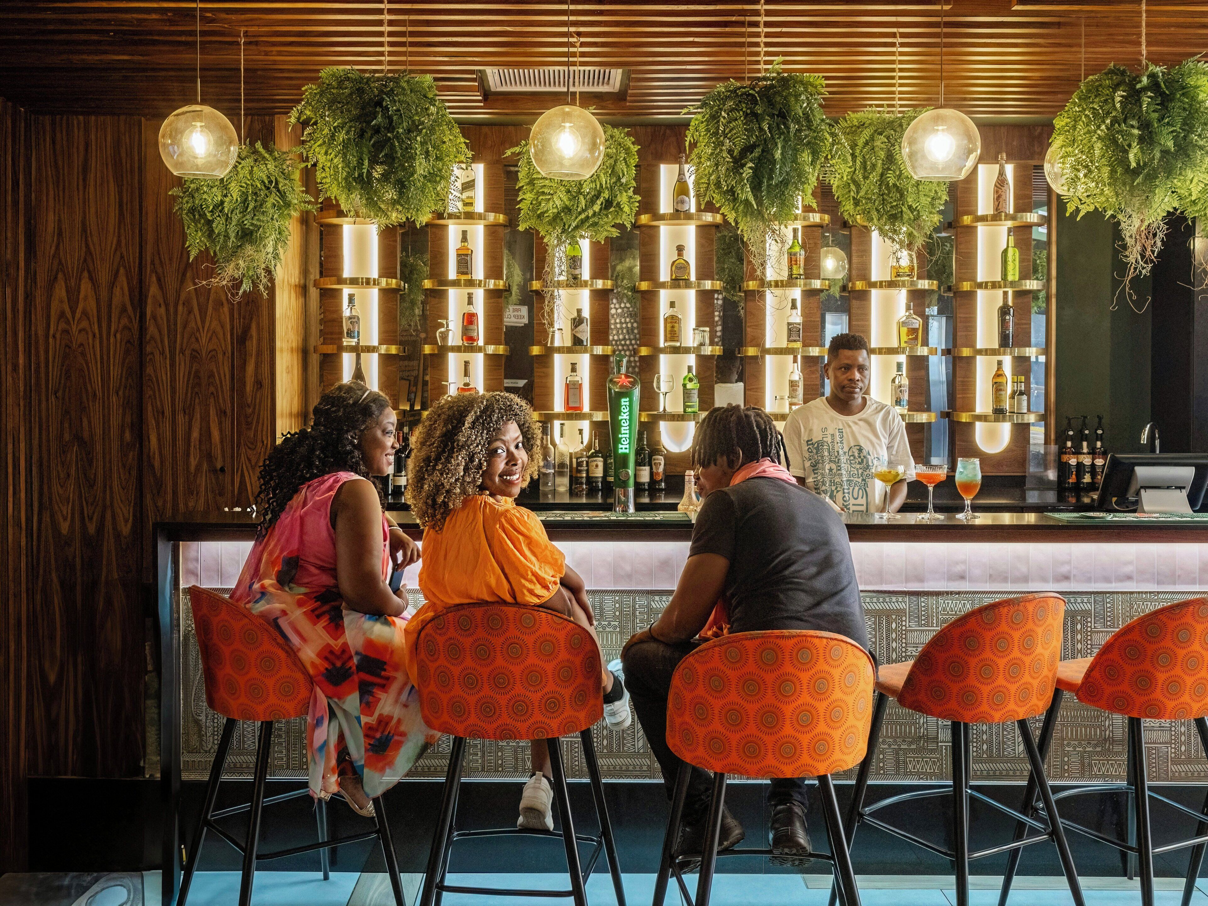 Een bar met houten lambrisering, hangplanten en een bartender.