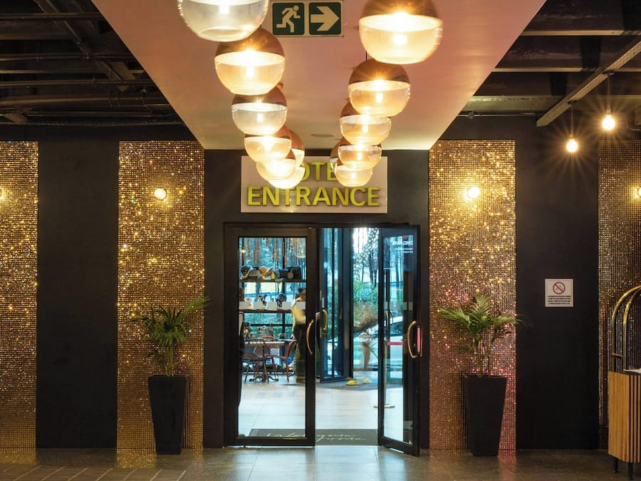 Entrada de un hotel con un cartel, una escalera y un paso de peatones.