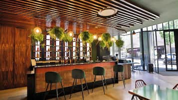 Zona de bar con techo de listones de madera, plantas colgantes y taburetes de bar.