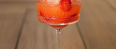 Un cóctel en un vaso de tallo con hielo y una fresa como decoración sobre una superficie de madera.