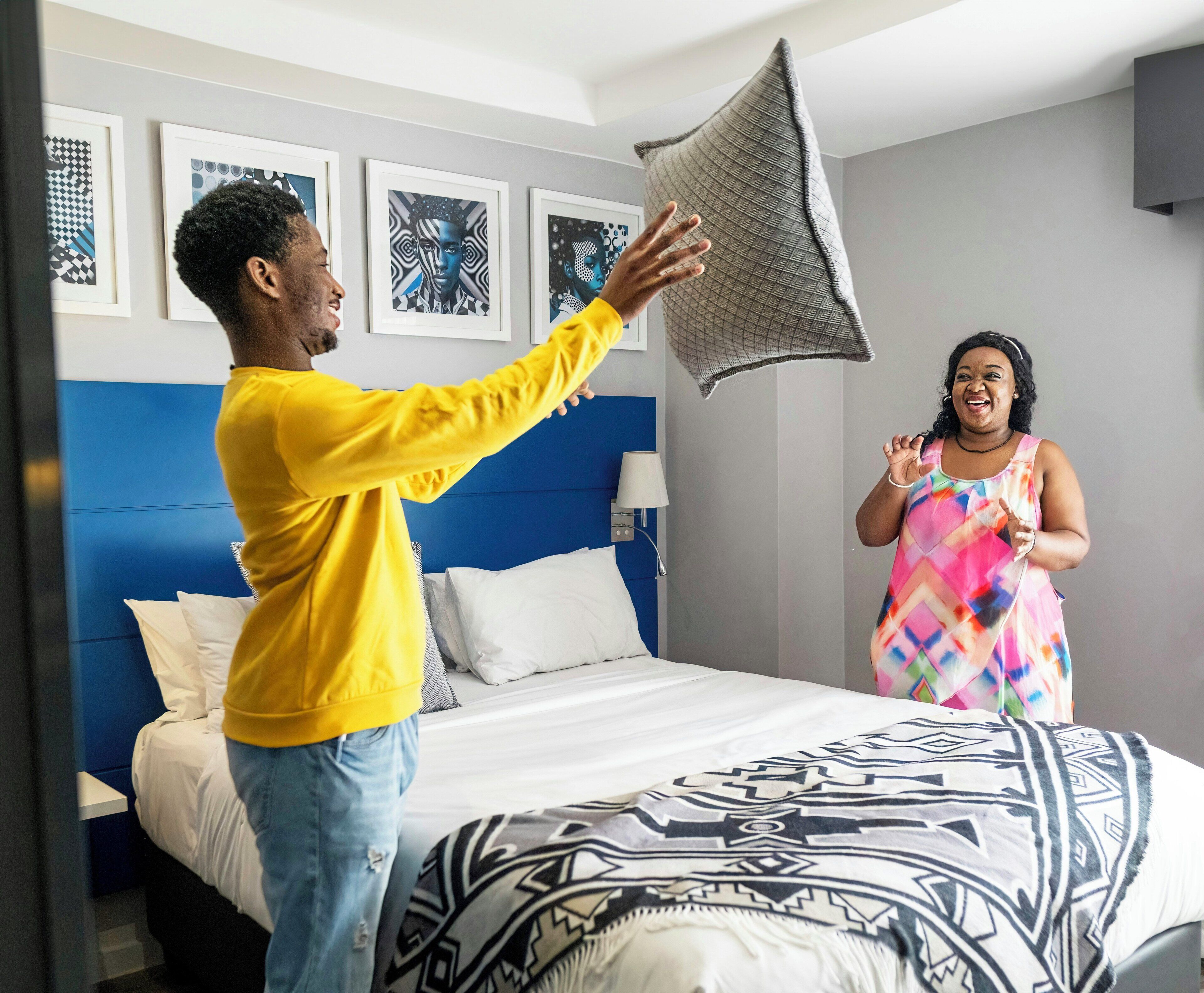 A hotel room with a bed, a blue headboard, and a wall with framed artwork.