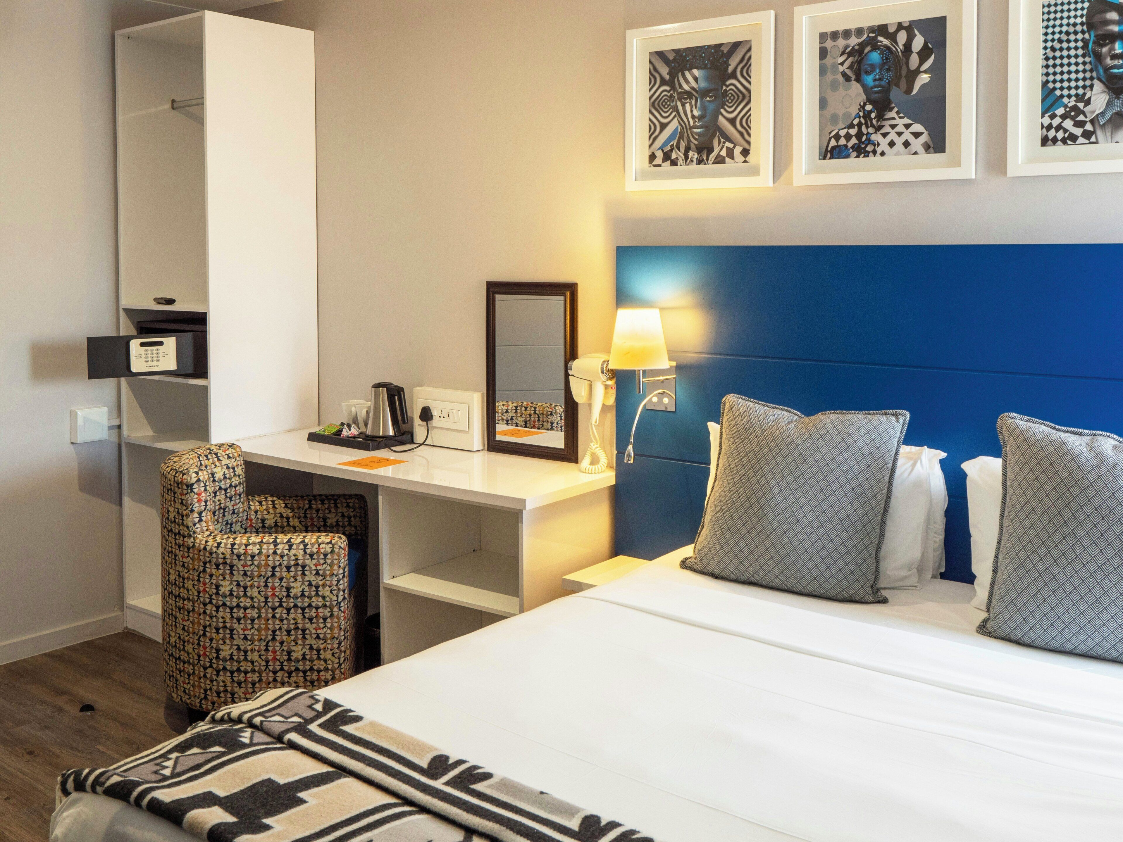 Habitación de hotel con cama, escritorio, silla, espejo y obras de arte en la pared.