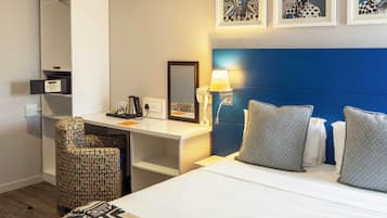 Habitación de hotel con cama, escritorio, silla, espejo y obras de arte en la pared.