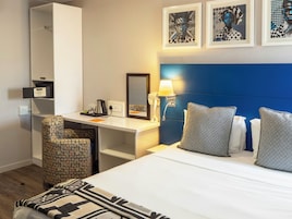 Habitación de hotel con cama, escritorio, silla, espejo y obras de arte en la pared.