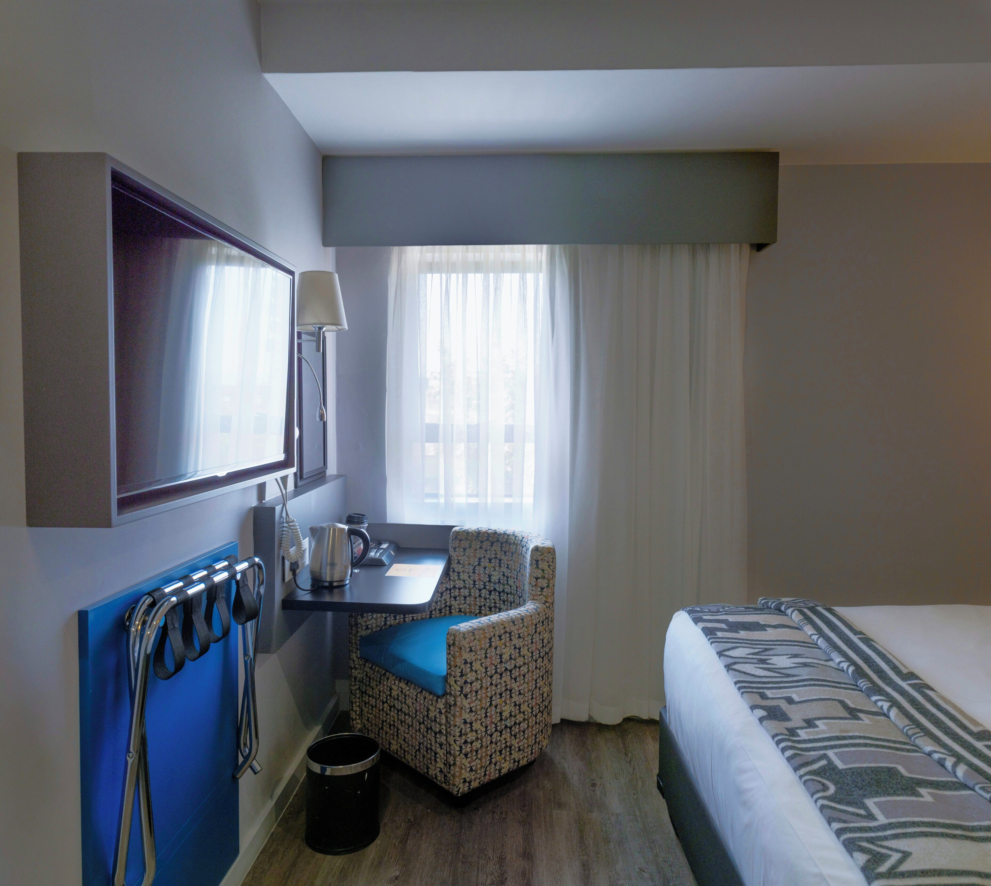 Habitación de hotel con cama, escritorio, silla, televisión y ventana con cortinas.