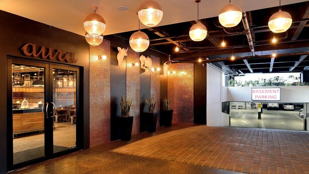 A modern interior with a 'Aura' sign, potted plants, and a 'Basement Parking' sign. - ONOMO Hotel Johannesburg Sandton (Sandton)