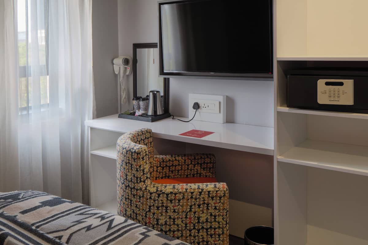Une chambre d’hôtel équipée d’un lit, d’un téléviseur fixé au mur, d’un sèche-cheveux et d’une machine à café posée sur une étagère.