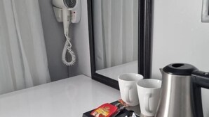 A hotel room with a white countertop, a hairdryer, a mirror, two white mugs, a silver coffee pot, and a tray with tea bags and a red packet. - ONOMO Hotel Johannesburg Sandton (Sandton)